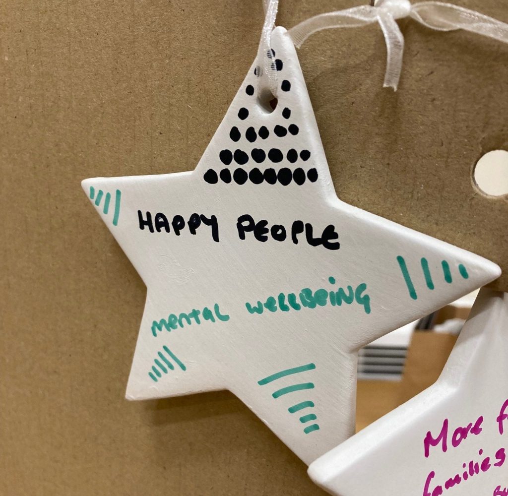 A hand-decorated ceramic star with the message "Happy people, emotional wellbeing" written across it