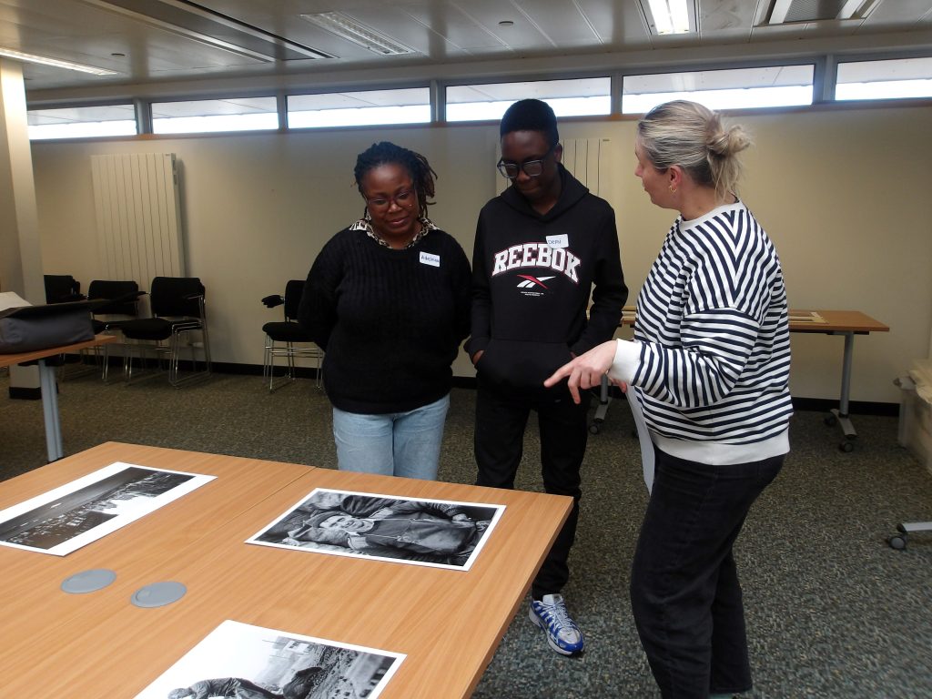 Two women and a teenage boy look at black and white archive photographs on a table