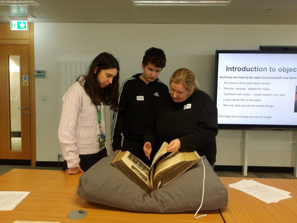Three people - two women and a teenage boy - look at an old book nestled on a large cushion