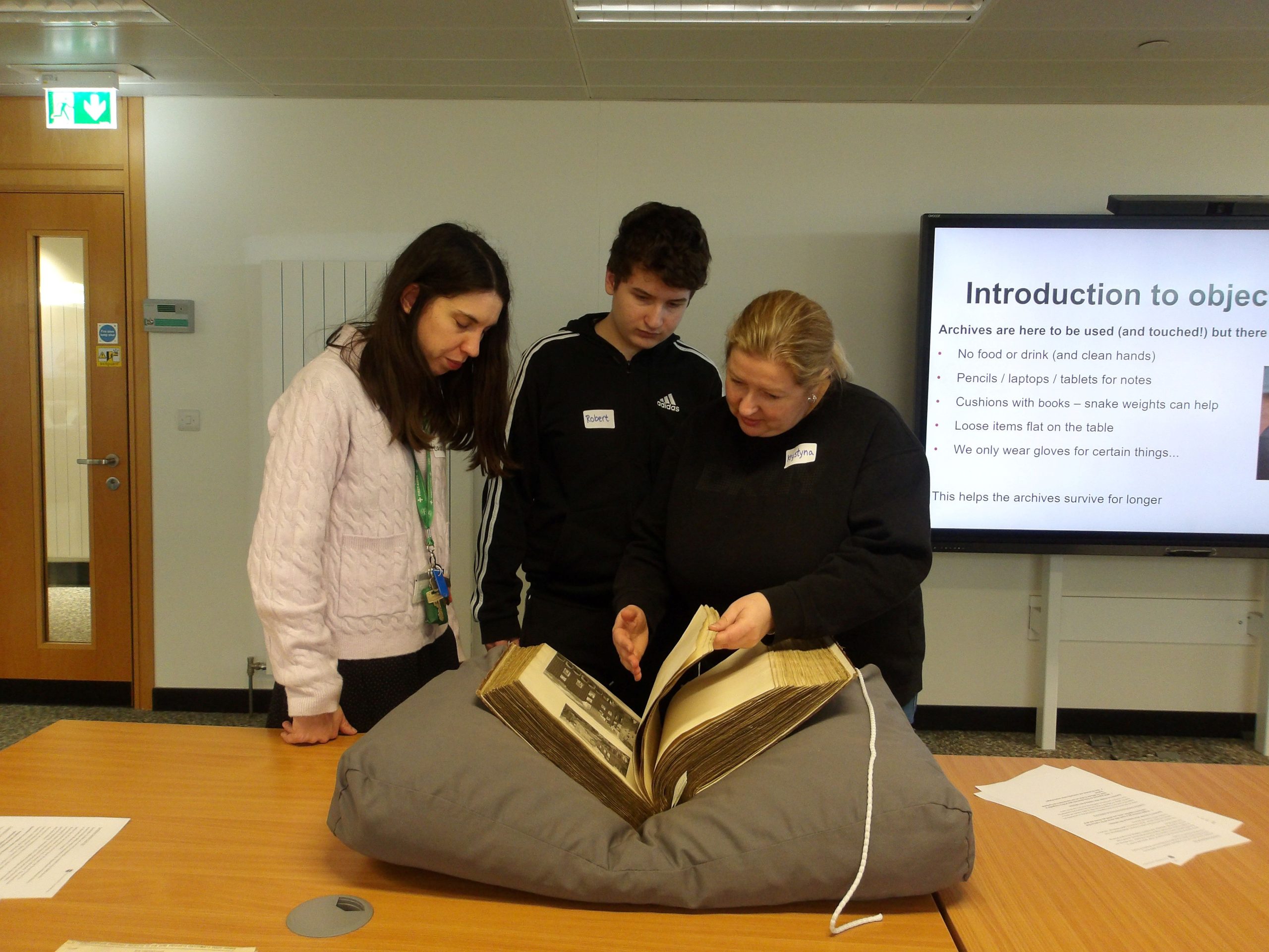 Three people - two women and a teenage boy - look at an old book nestled on a large cushion