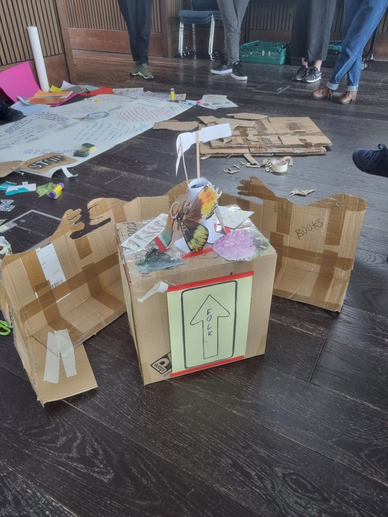 Photo shows lots of cardboard structure taped together on a floor, with paper strewn in the background